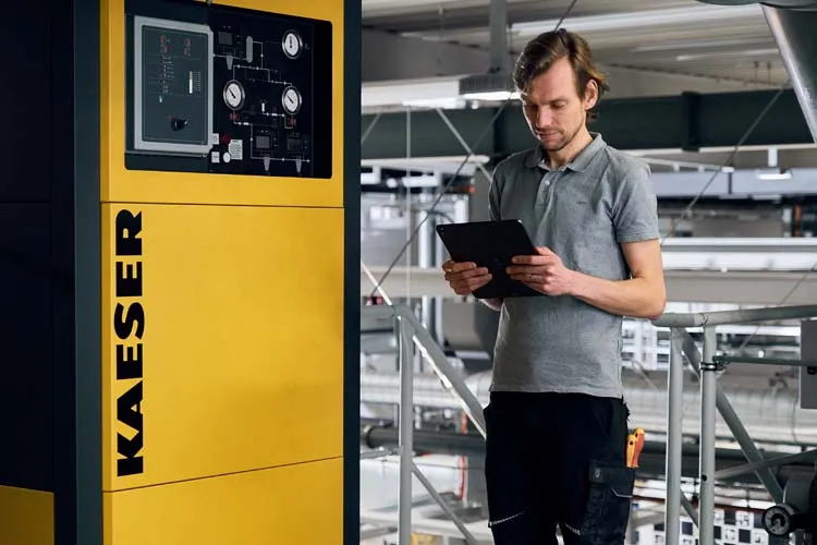 Ein Instandhaltungsmitarbeiter steht mit Tablet in der Hand an einer Anlage und dokumentiert die Instandhaltungsaufträge.